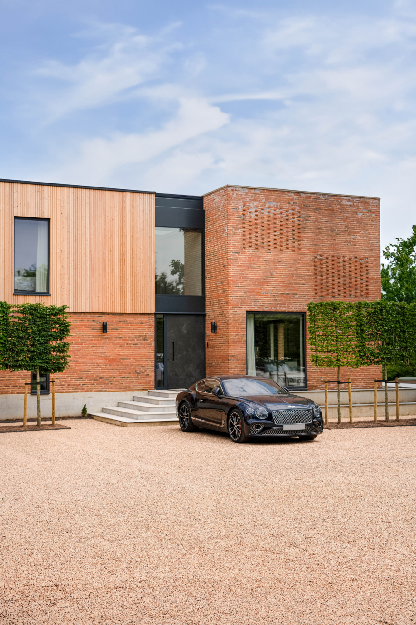 Bentley parked on a gravel driveway outside a contemporary home