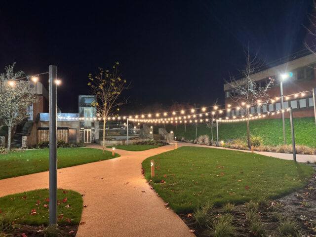 Illuminated curved path beside the lawn at Booths Park courtyard.